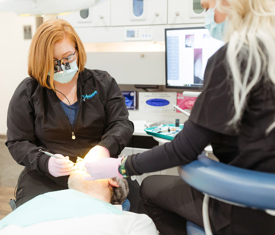 Staff members working on a patient's mouth in dental chair